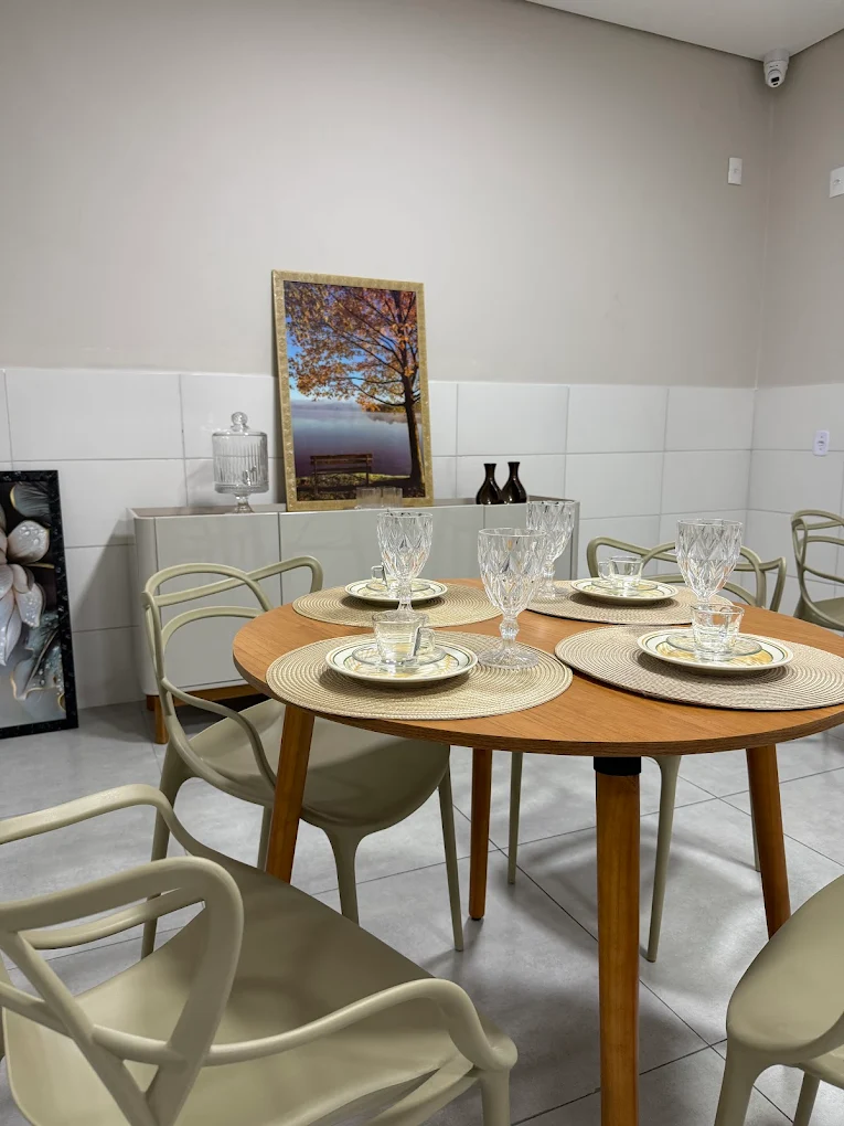 Mesa de jantar redonda em madeira com taças de cristal e cadeiras claras
